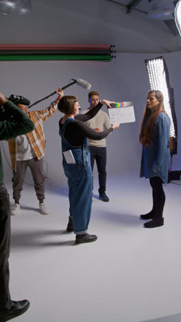 Vertical-Video-Of-Frustrated-Female-Assistant-Using-Clapperboard-As-Actors-Shoot-Movie-Or-Video-In-Studio-With-Film-Crew-And-Director-Shot-In-Real-Time